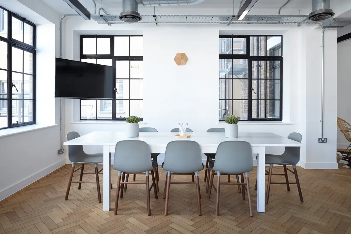 Bright office interior with a white conference table, grey chairs and herringbone wood floor