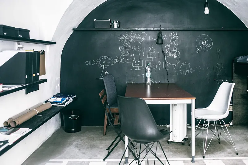 Studio workspace with a chalkboard wall, shelves of binders and rolled drawings